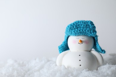 Photo of Cute decorative snowman on artificial snow against light background. Space for text