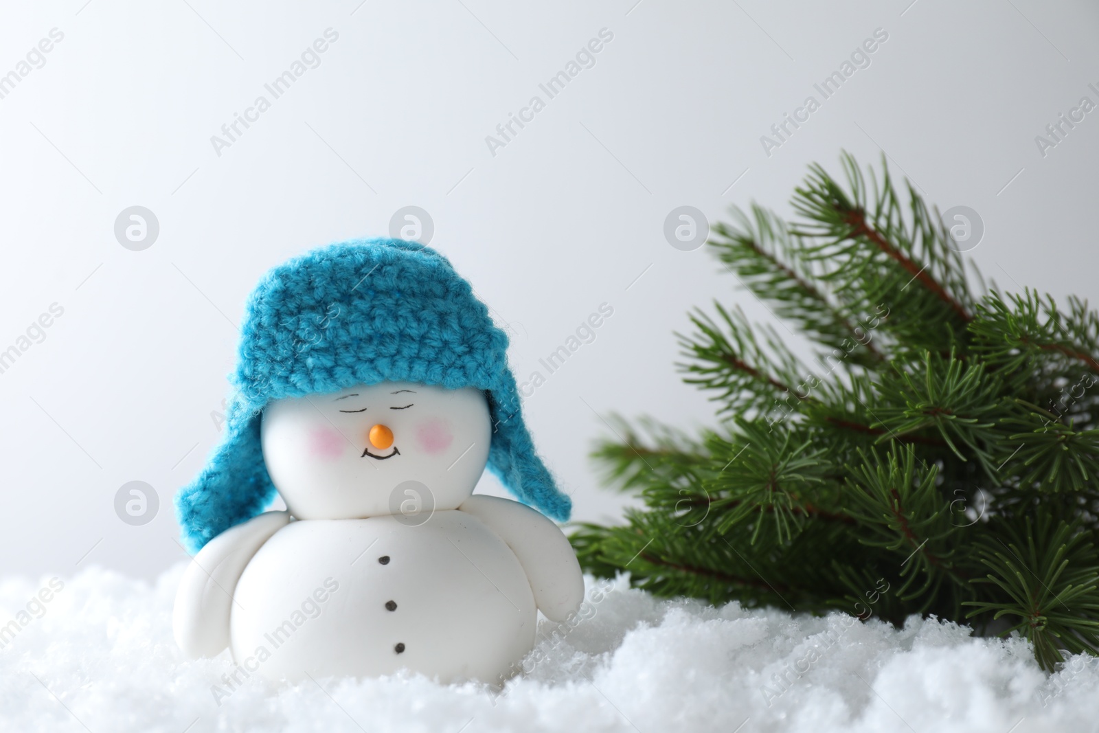 Photo of Cute decorative snowman and fir branches on artificial snow against light background