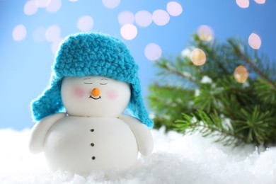 Photo of Cute decorative snowman and fir branches on artificial snow against blurred lights, closeup