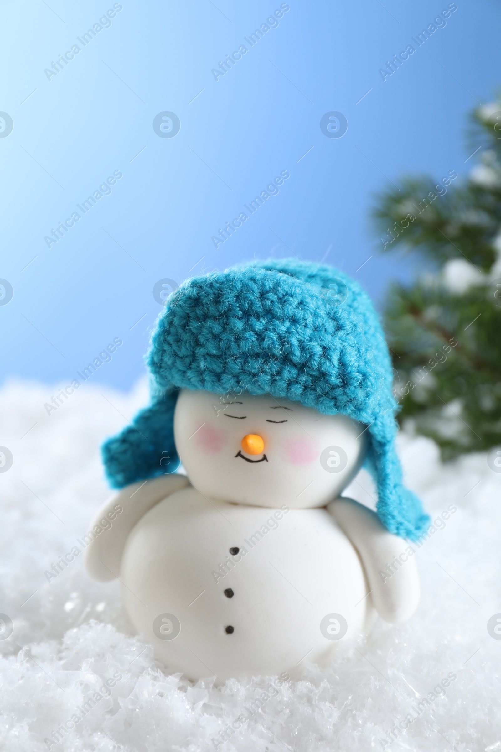 Photo of Cute decorative snowman on artificial snow against light blue background