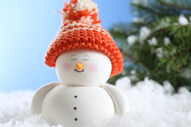 Cute decorative snowman on artificial snow against light blue background, closeup