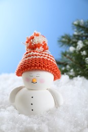 Photo of Cute decorative snowman on artificial snow against light blue background