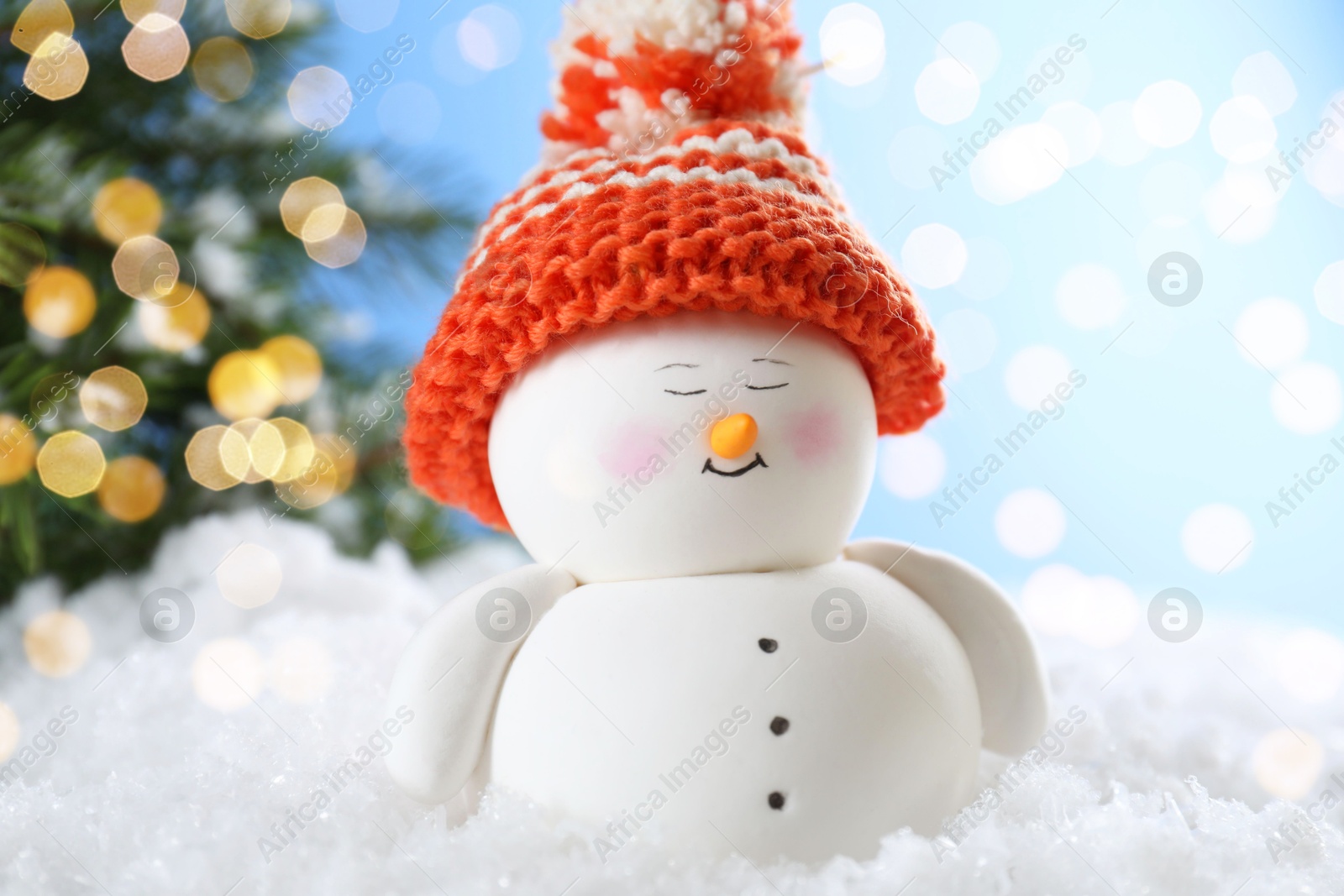 Photo of Cute decorative snowman on artificial snow against blurred lights, closeup