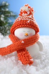 Photo of Cute decorative snowman on artificial snow against light blue background, closeup