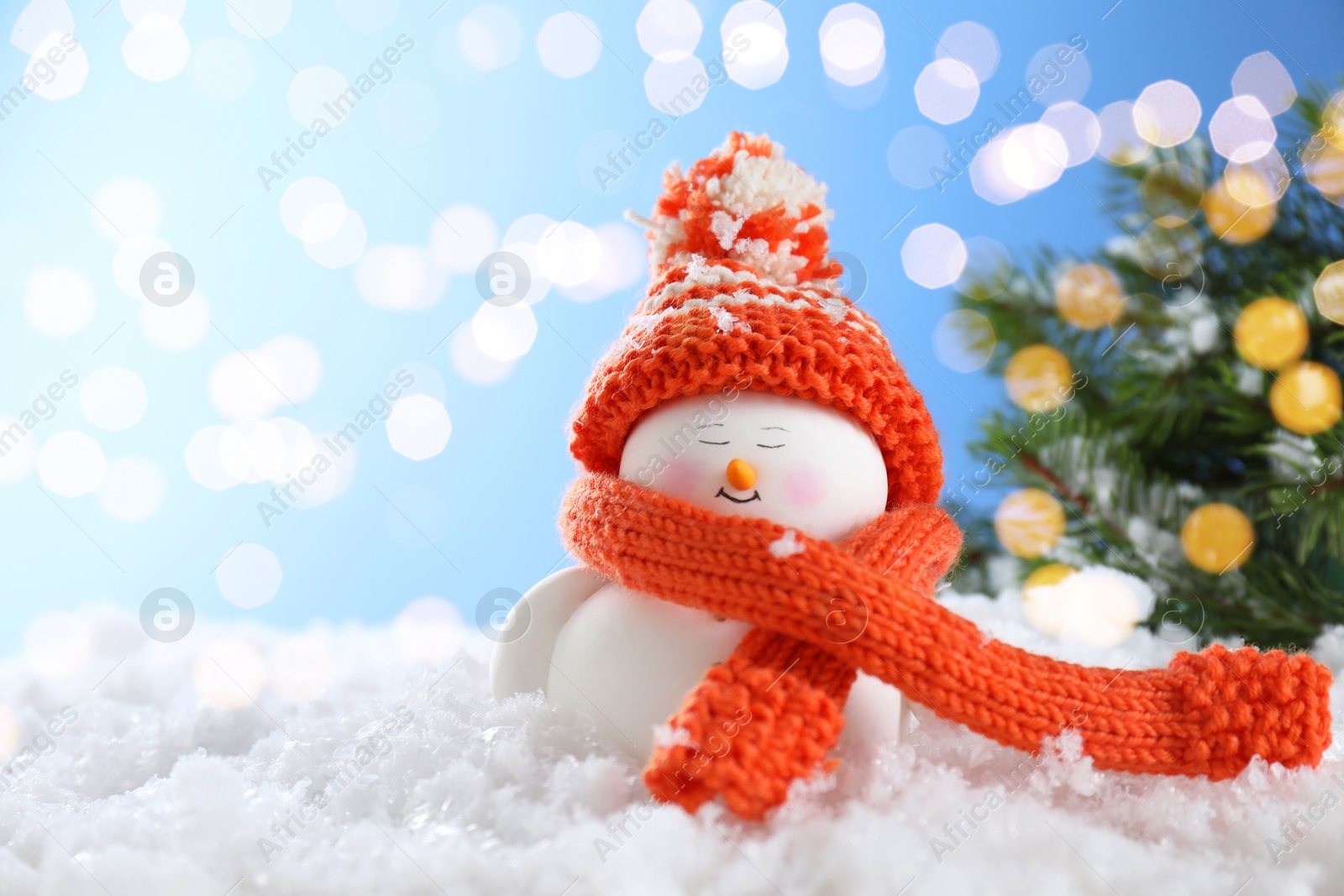 Photo of Cute decorative snowman on artificial snow against blurred lights. Space for text