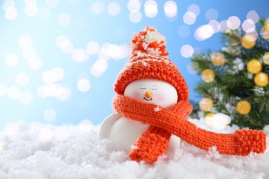 Photo of Cute decorative snowman on artificial snow against blurred lights. Space for text