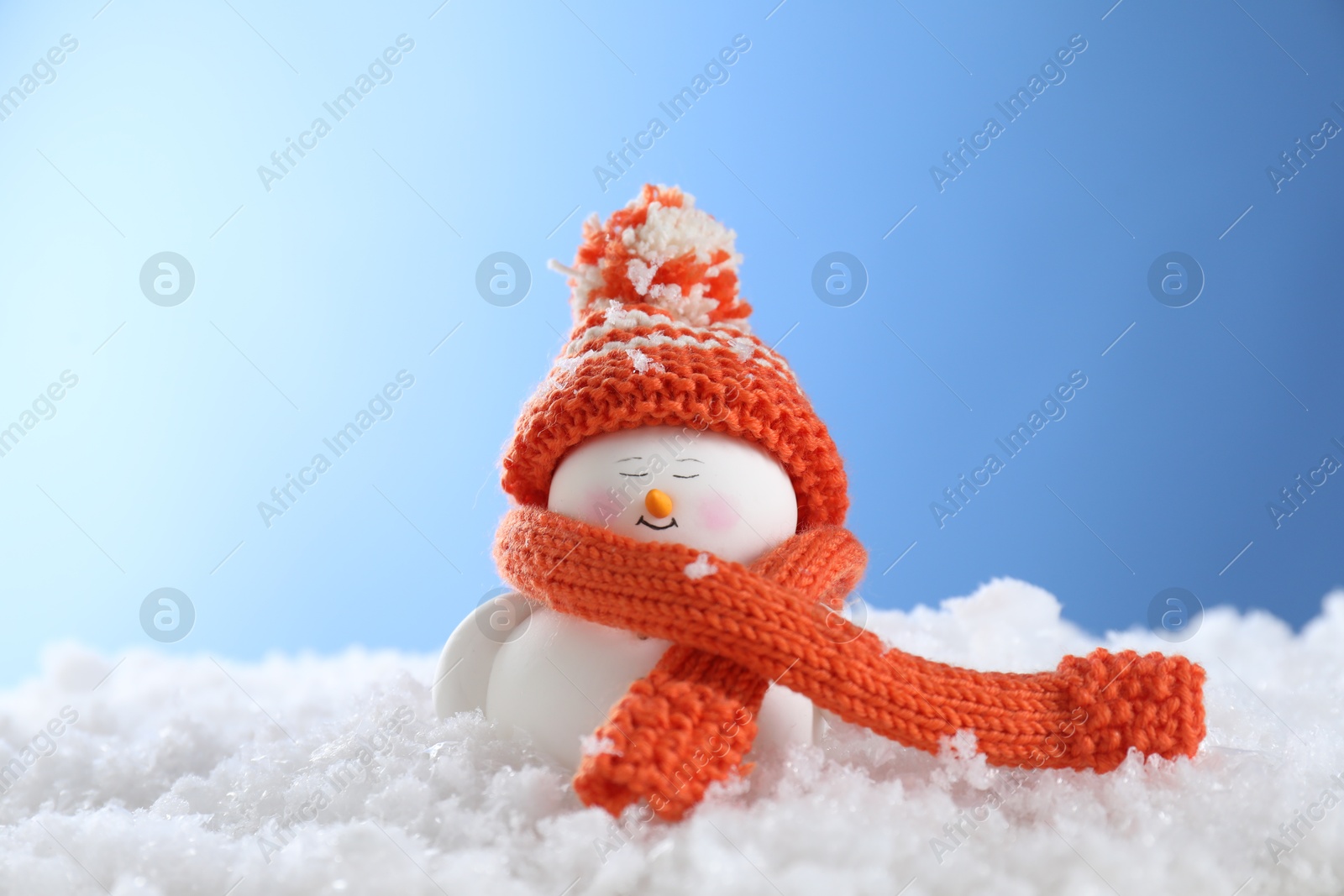 Photo of Cute decorative snowman on artificial snow against light blue background