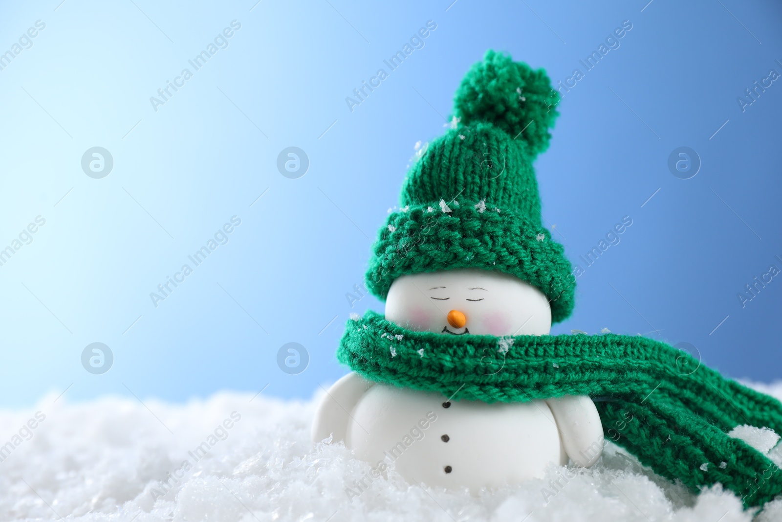 Photo of Cute decorative snowman on artificial snow against light blue background. Space for text