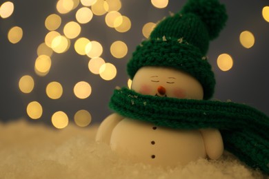 Photo of Cute decorative snowman on artificial snow against blurred lights, closeup. Space for text