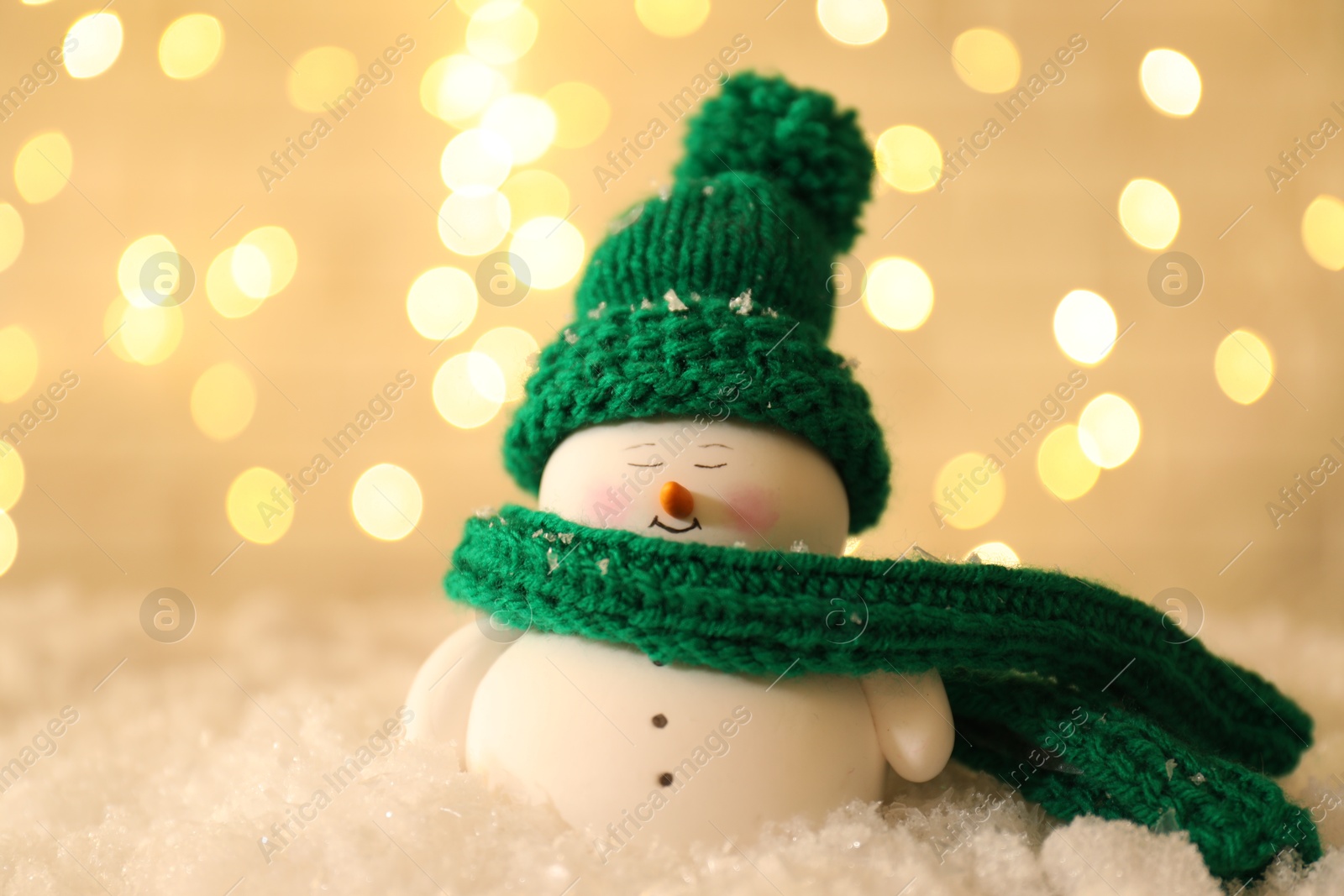 Photo of Cute decorative snowman on artificial snow against blurred lights, closeup