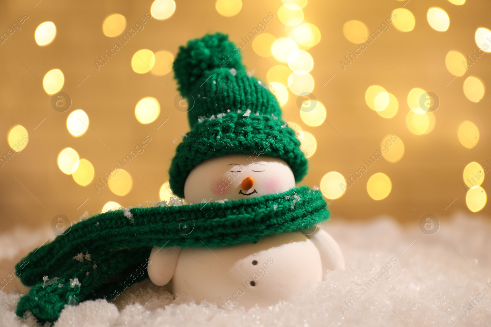 Photo of Cute decorative snowman on artificial snow against blurred lights, closeup