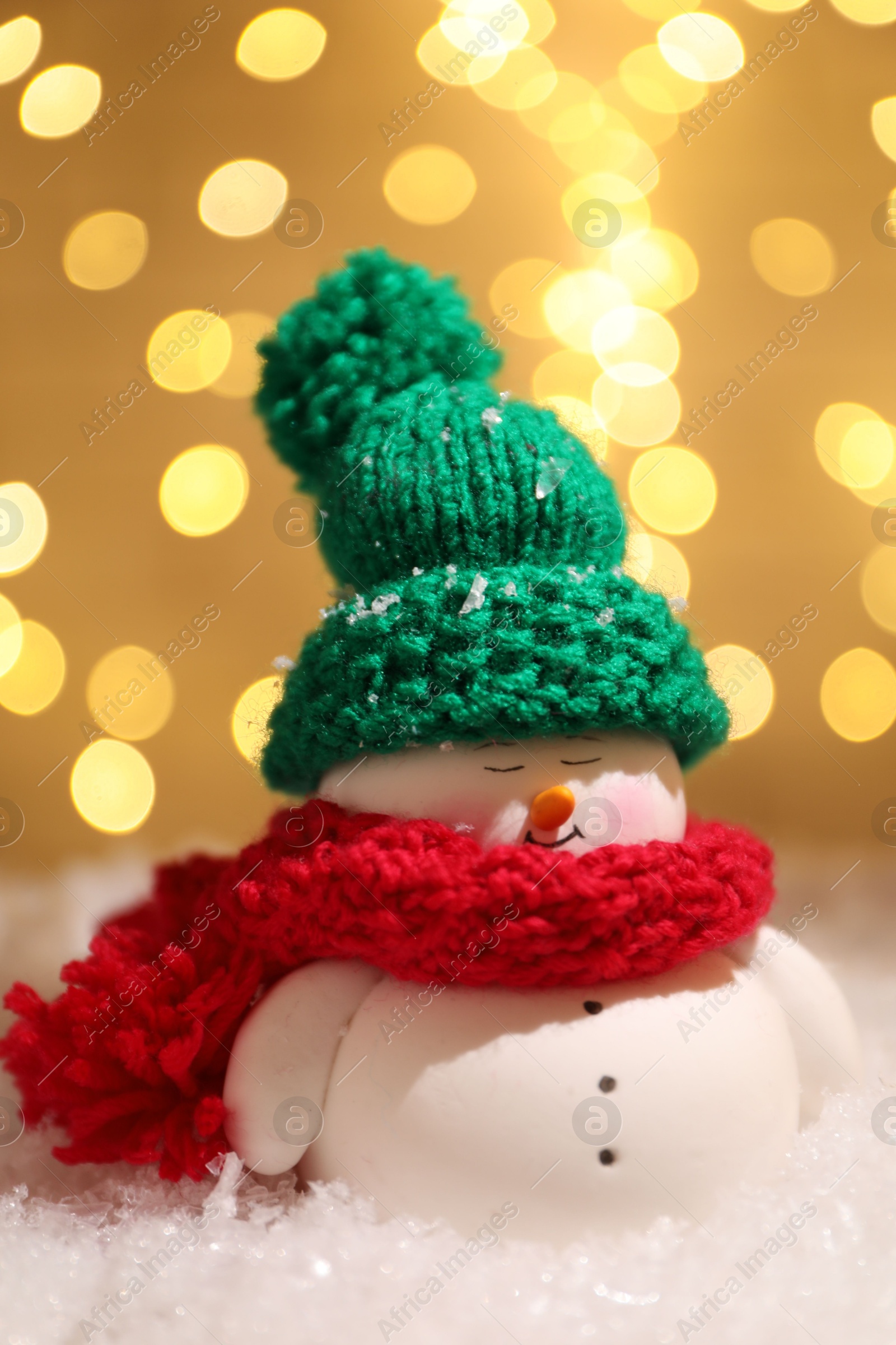 Photo of Cute decorative snowman on artificial snow against blurred lights, closeup