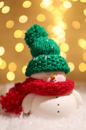 Photo of Cute decorative snowman on artificial snow against blurred lights, closeup