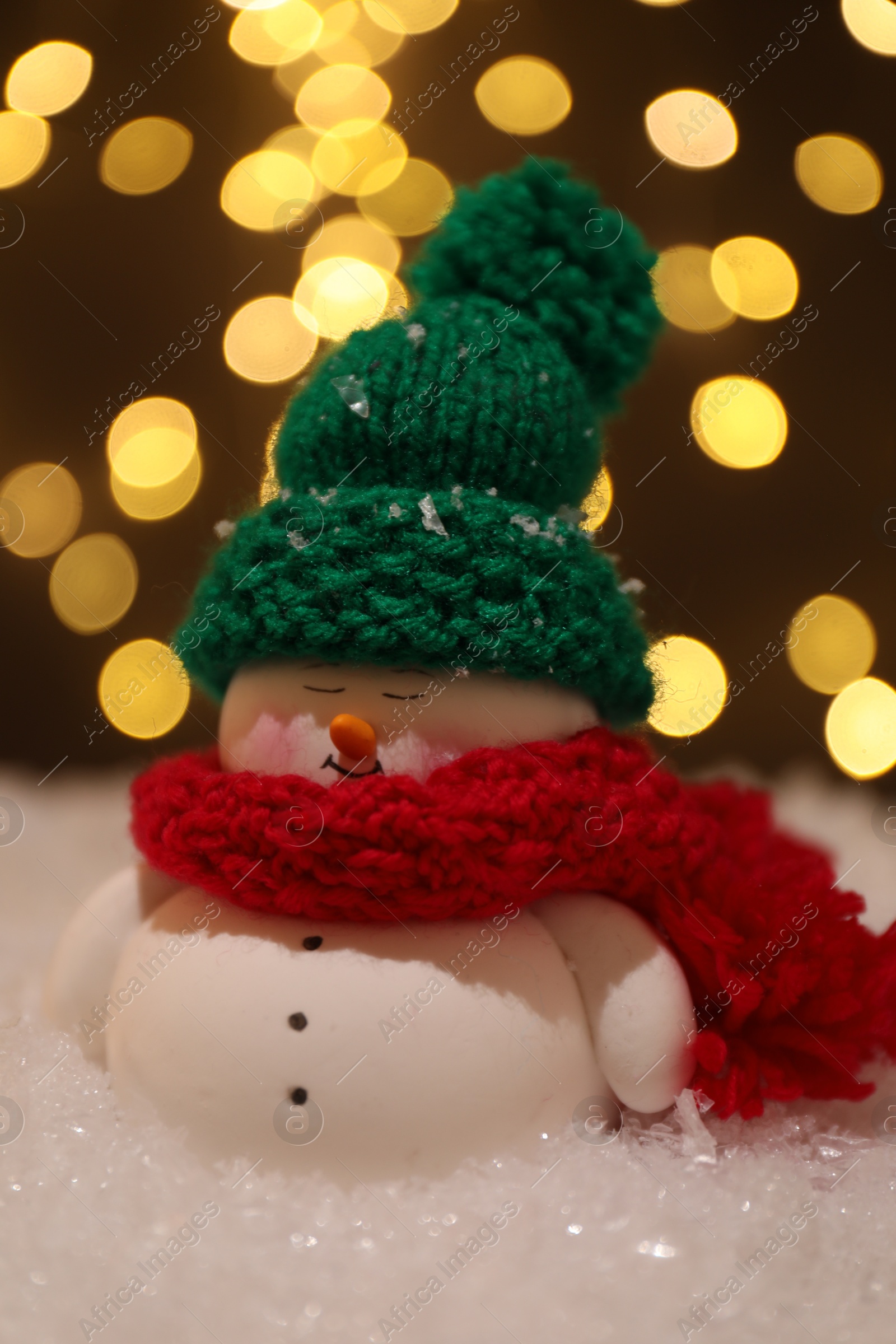 Photo of Cute decorative snowman on artificial snow against blurred lights, closeup