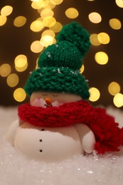 Photo of Cute decorative snowman on artificial snow against blurred lights, closeup