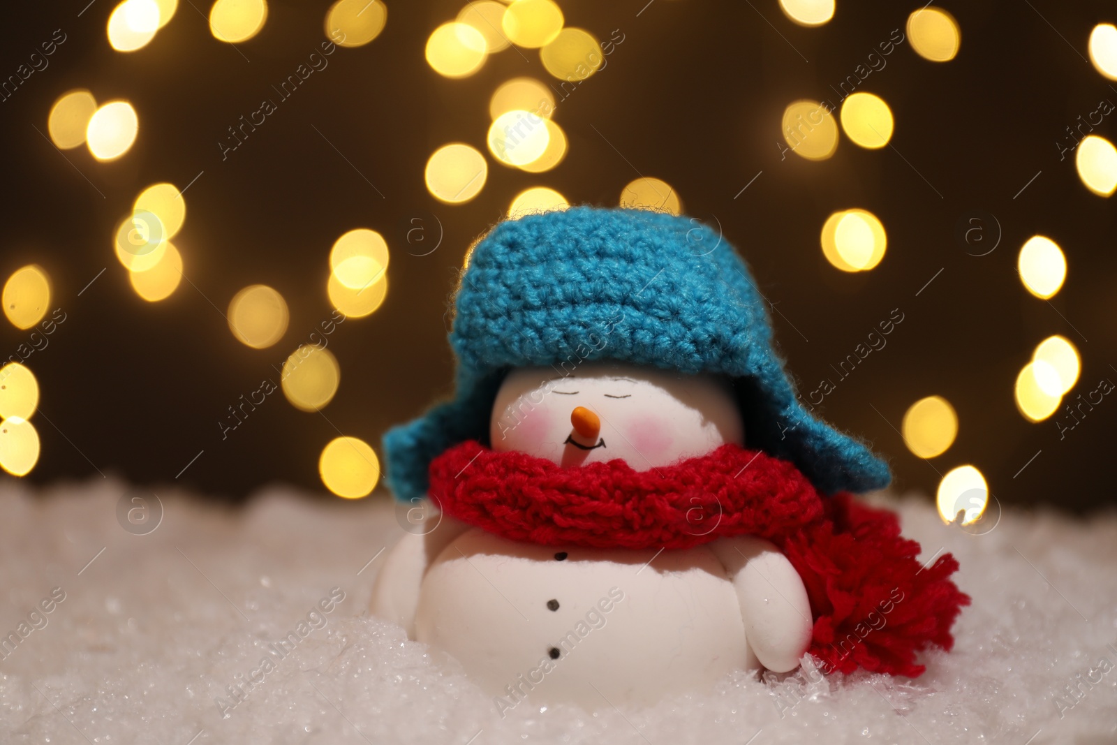 Photo of Cute decorative snowman on artificial snow against blurred lights, closeup