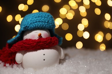 Photo of Cute decorative snowman on artificial snow against blurred lights, closeup. Space for text