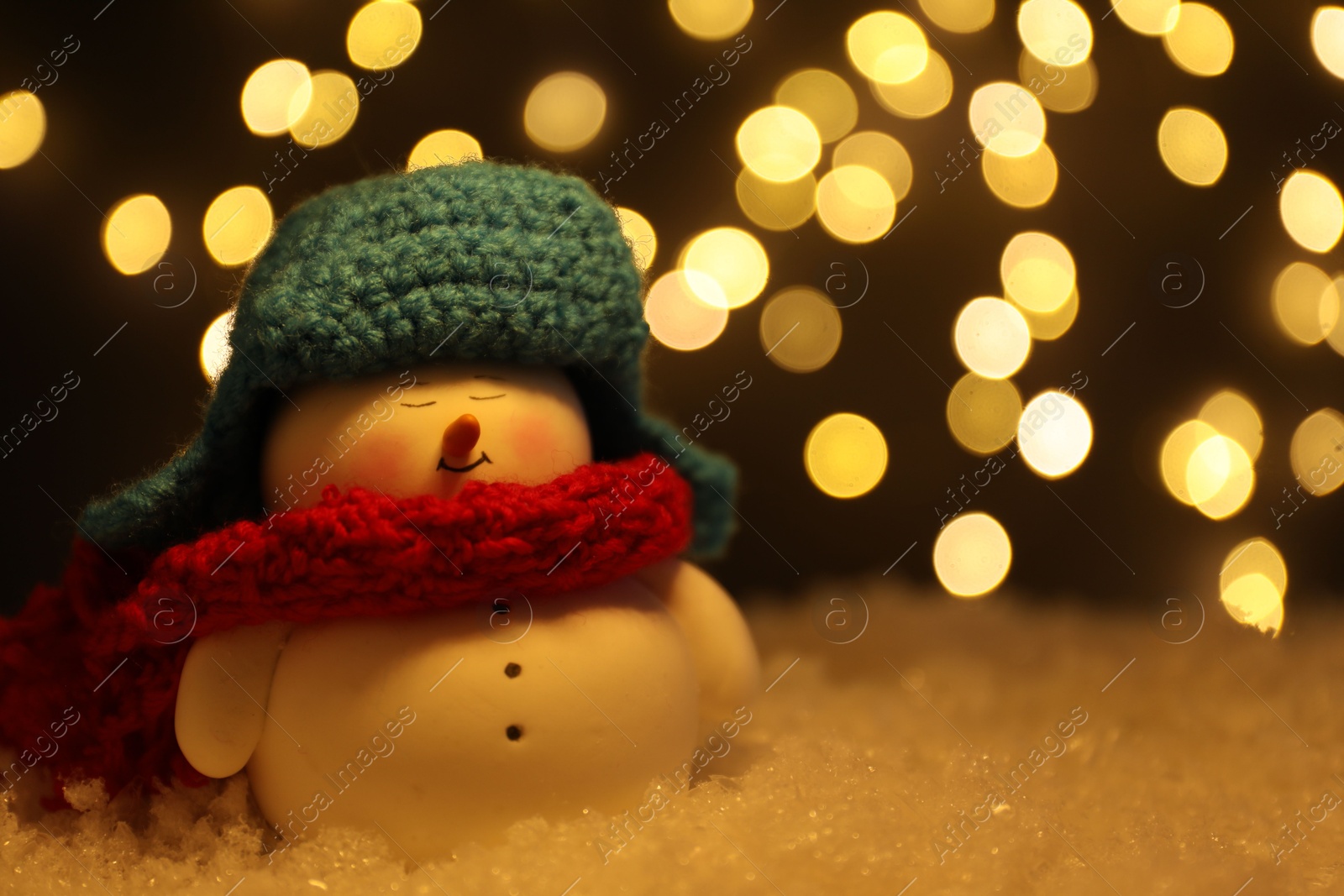 Photo of Cute decorative snowman on artificial snow against blurred lights, closeup. Space for text