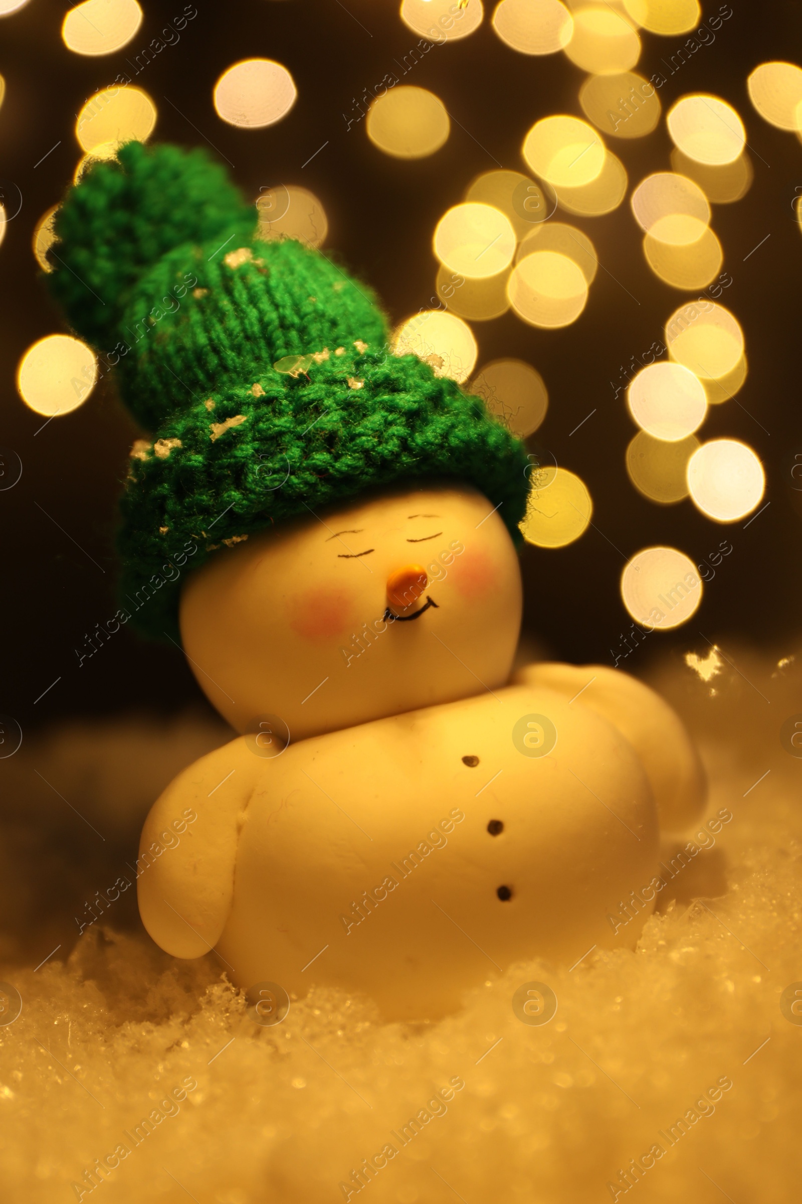 Photo of Cute decorative snowman on artificial snow against blurred lights, closeup