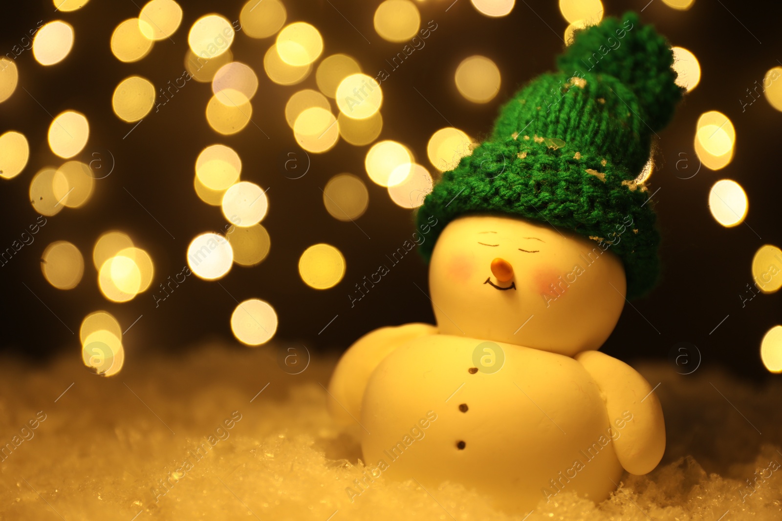 Photo of Cute decorative snowman on artificial snow against blurred lights, closeup. Space for text