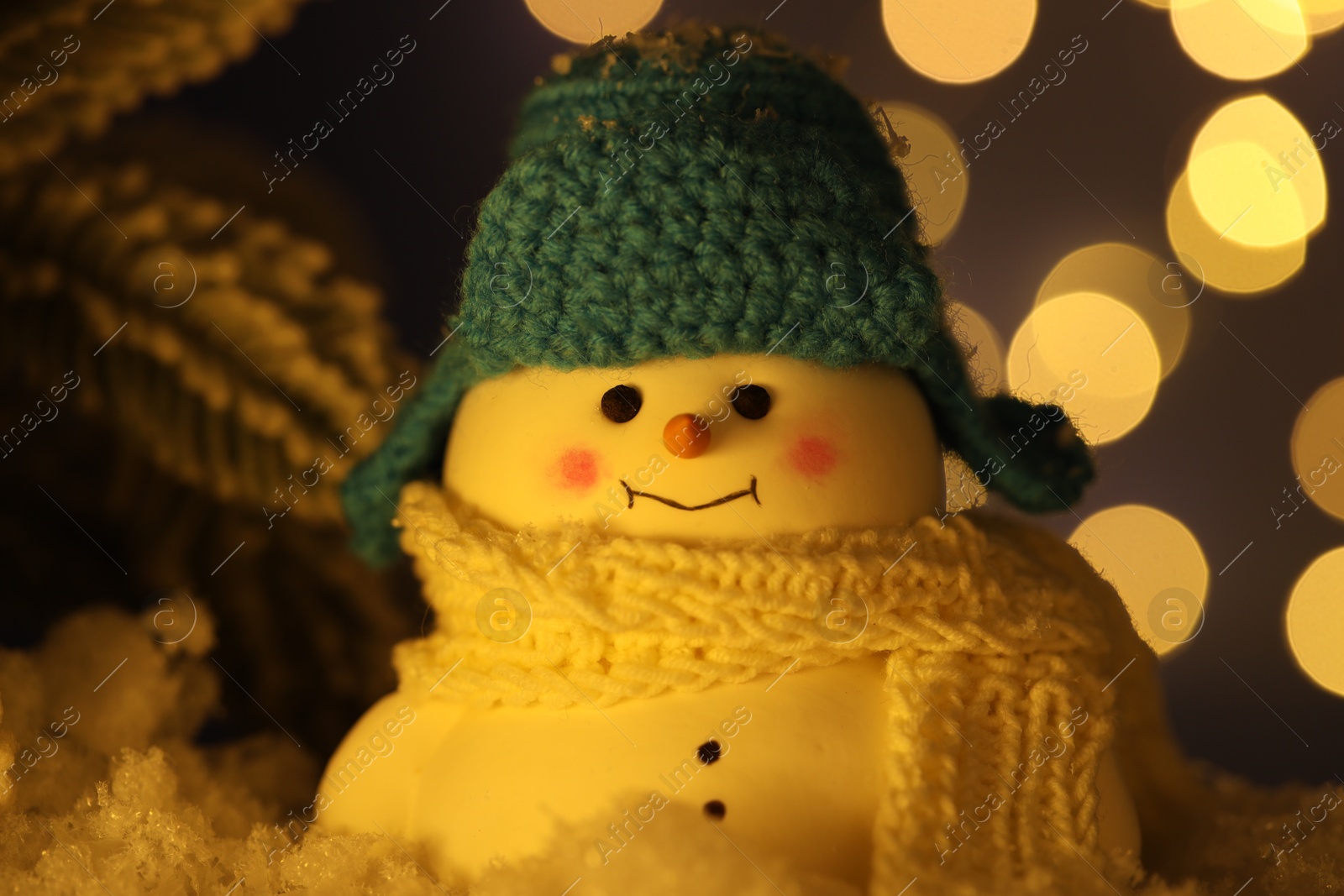 Photo of Cute decorative snowman on artificial snow against blurred lights, closeup