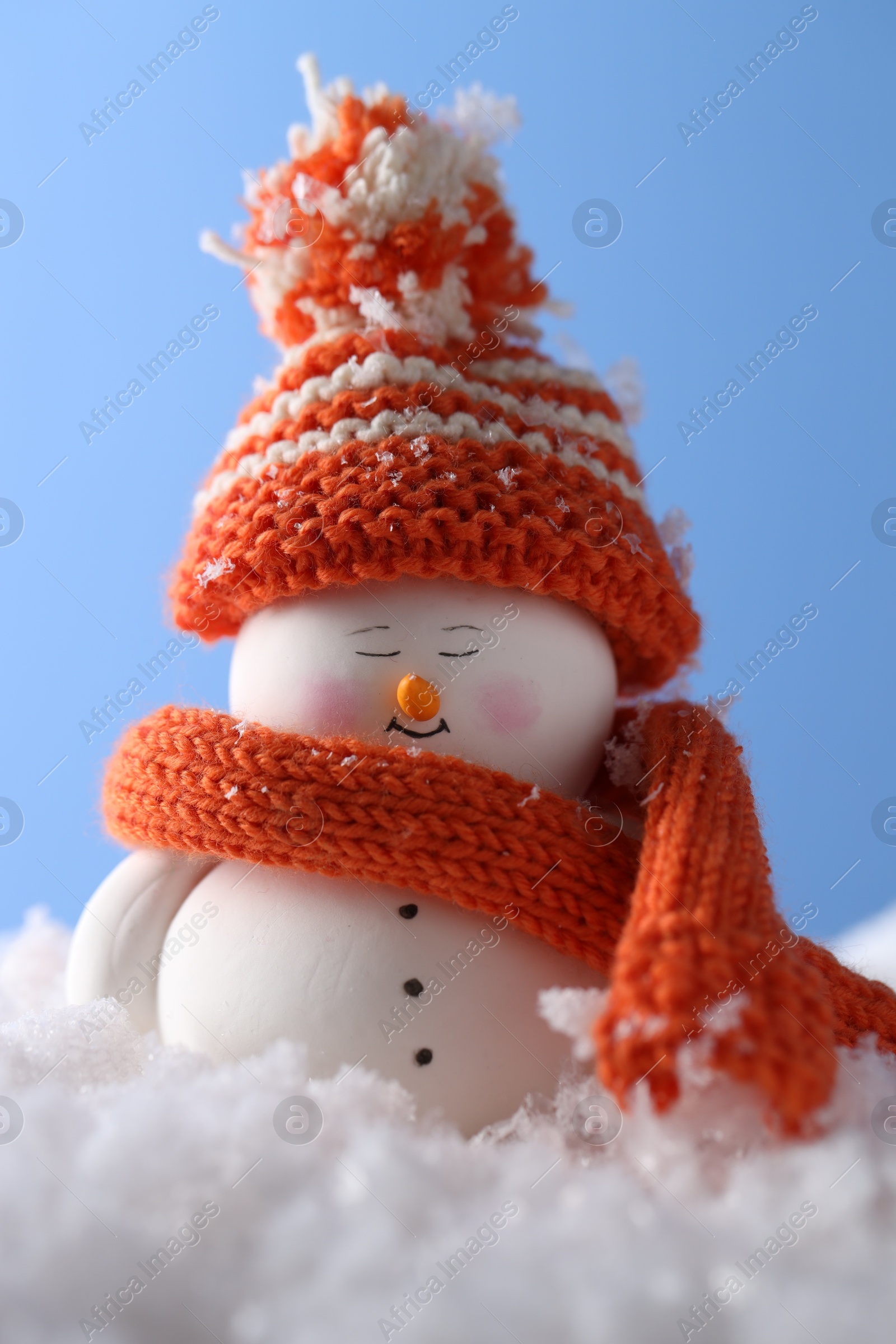 Photo of Cute decorative snowman on artificial snow against light blue background