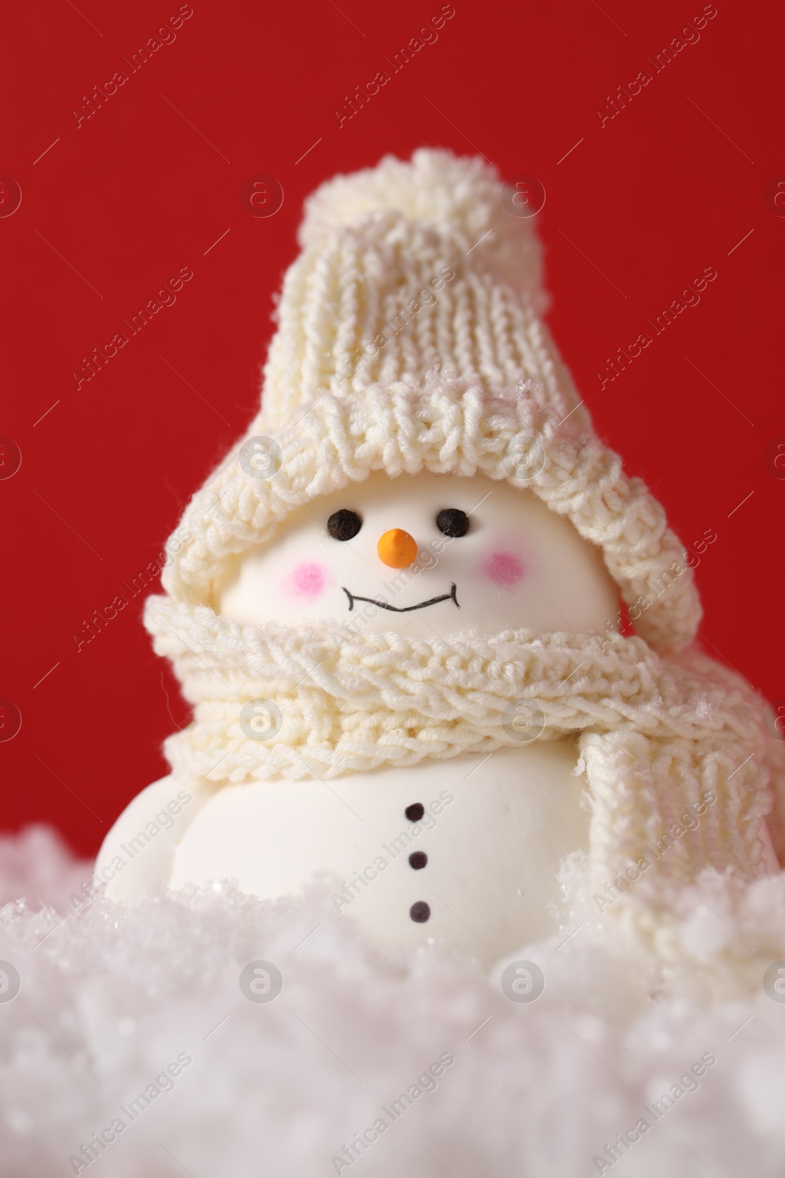 Photo of Cute decorative snowman on artificial snow against red background