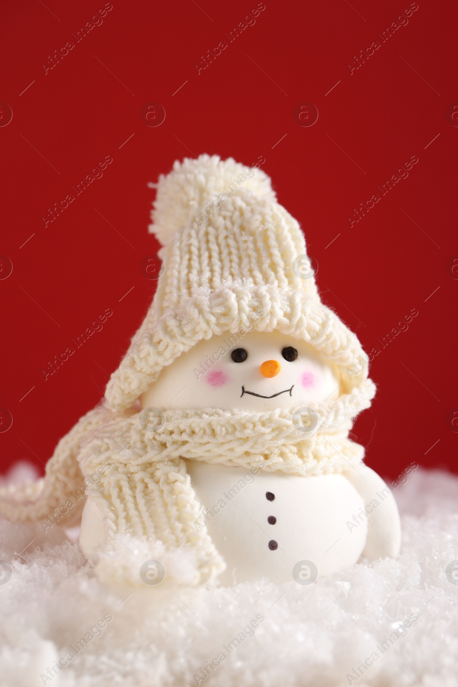 Photo of Cute decorative snowman on artificial snow against red background