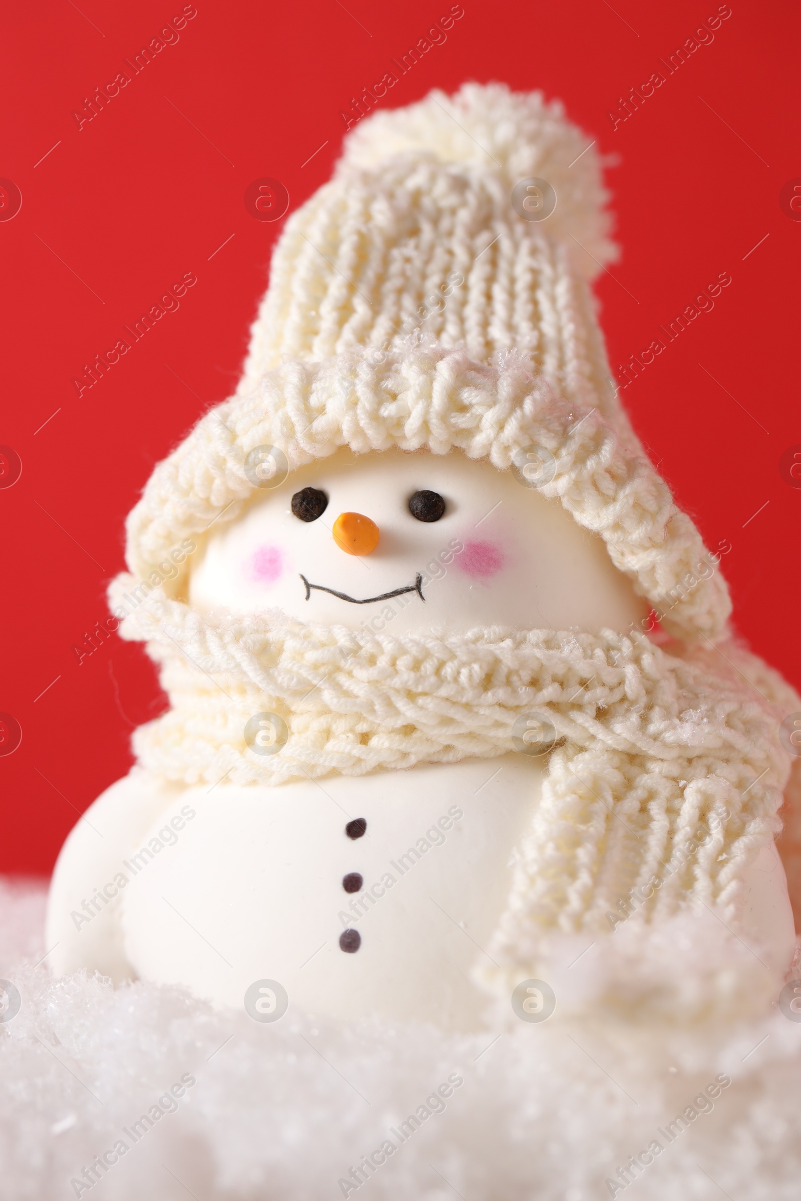 Photo of Cute decorative snowman on artificial snow against red background, closeup