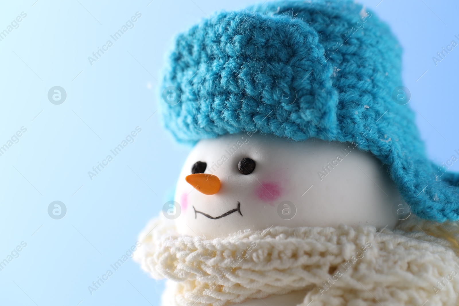 Photo of Cute decorative snowman against light blue background, closeup