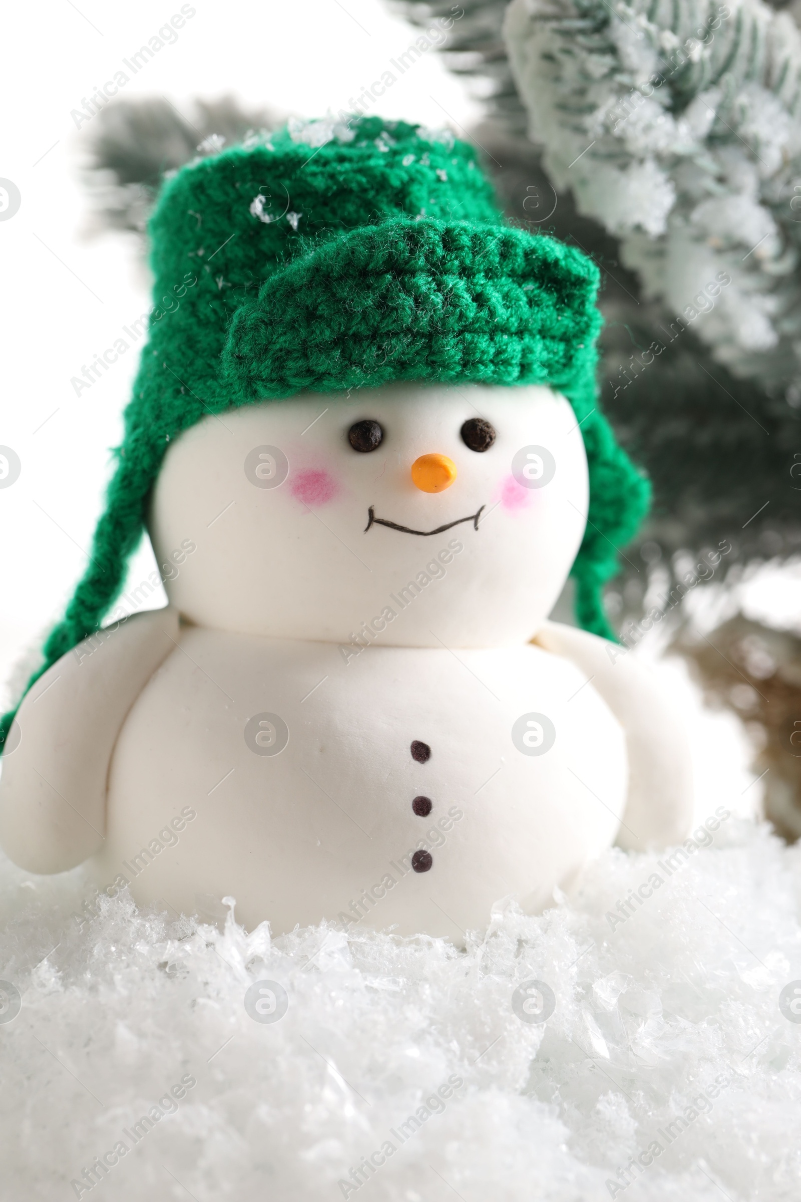 Photo of Cute decorative snowman and fir tree branches on artificial snow against white background, closeup