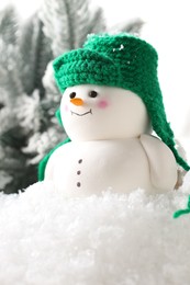 Photo of Cute decorative snowman and fir tree branches on artificial snow against white background, closeup