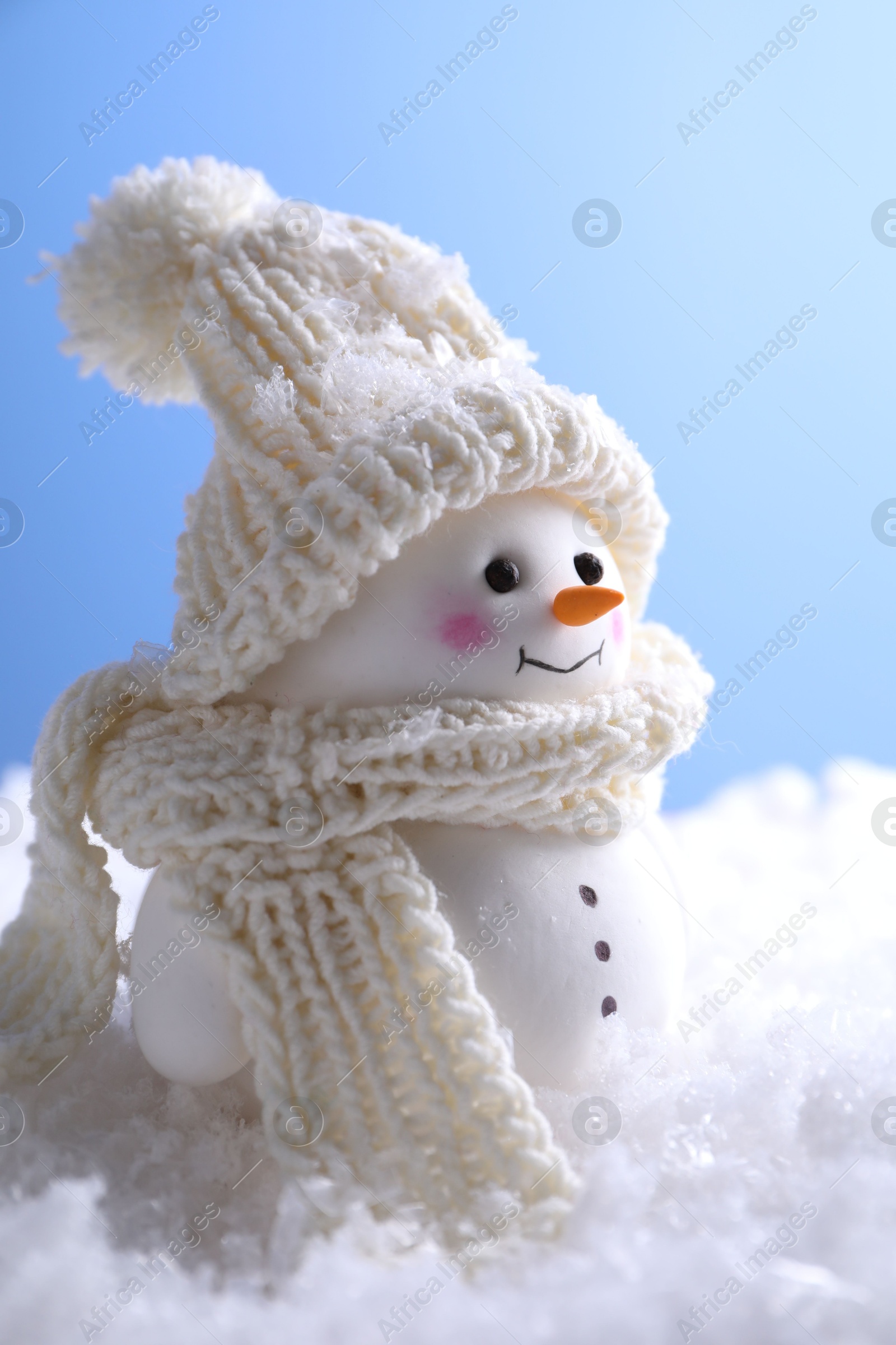 Photo of Cute decorative snowman on artificial snow against light blue background, closeup