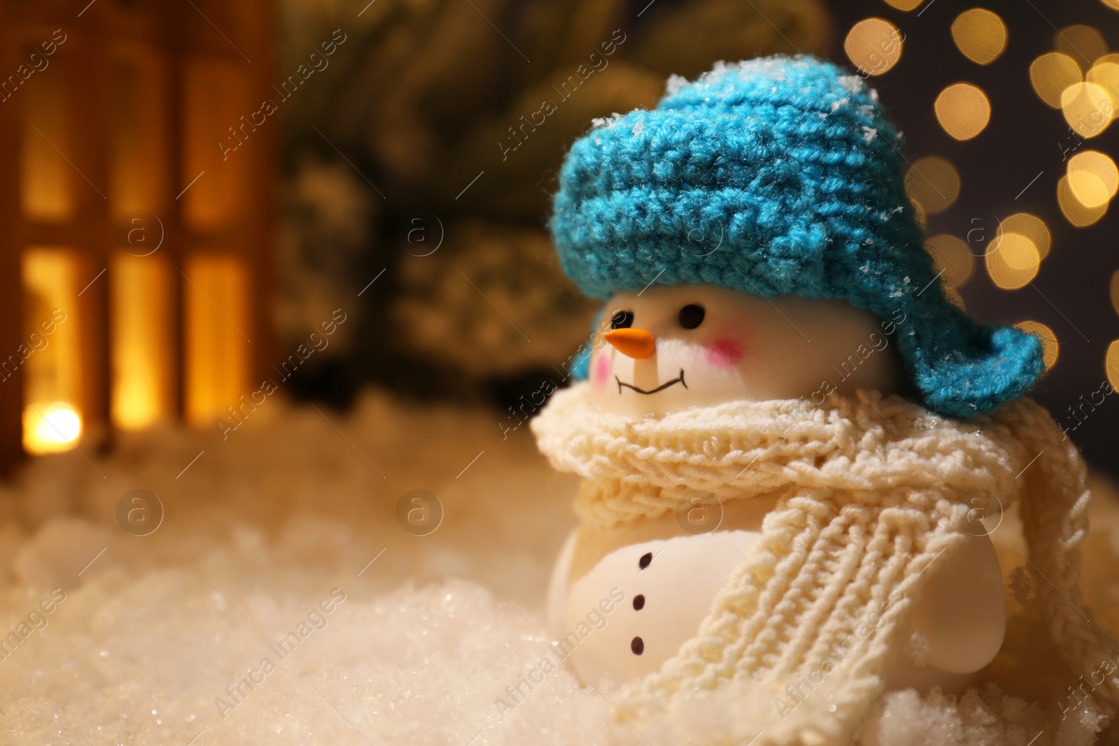 Photo of Cute decorative snowman and other decor on artificial snow against blurred lights, closeup