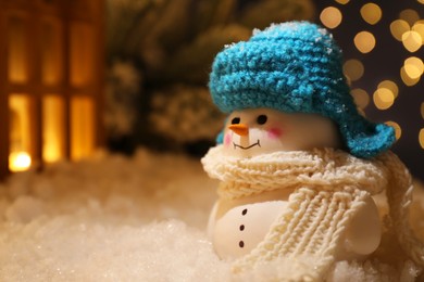 Photo of Cute decorative snowman and other decor on artificial snow against blurred lights, closeup