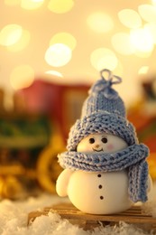 Photo of Cute decorative snowman on artificial snow against blurred lights, closeup