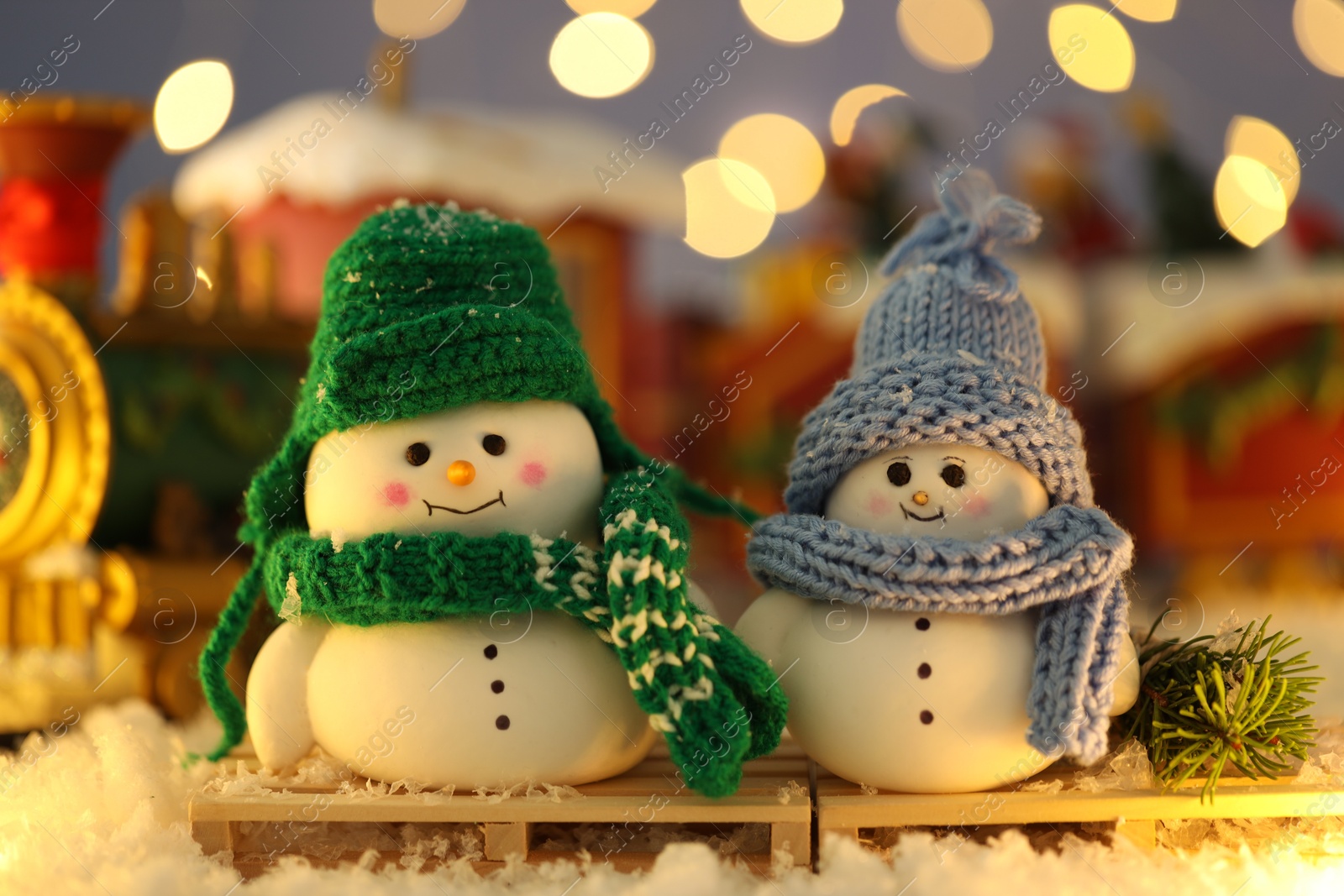 Photo of Cute decorative snowmen on artificial snow against blurred background, closeup