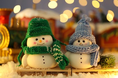 Photo of Cute decorative snowmen on artificial snow against blurred background, closeup