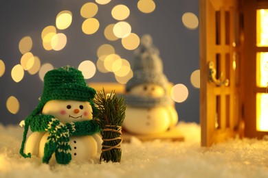 Photo of Cute decorative snowmen, fir tree branches and lantern on artificial snow against blurred lights, selective focus