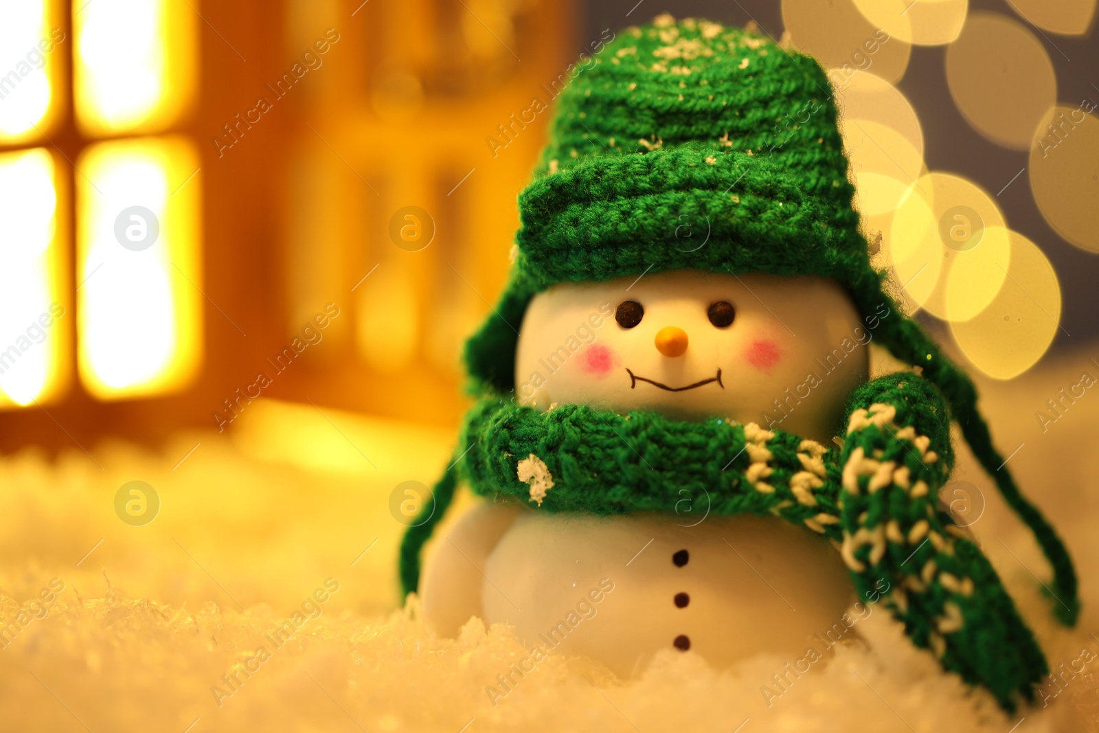 Photo of Cute decorative snowman on artificial snow against blurred lights, closeup