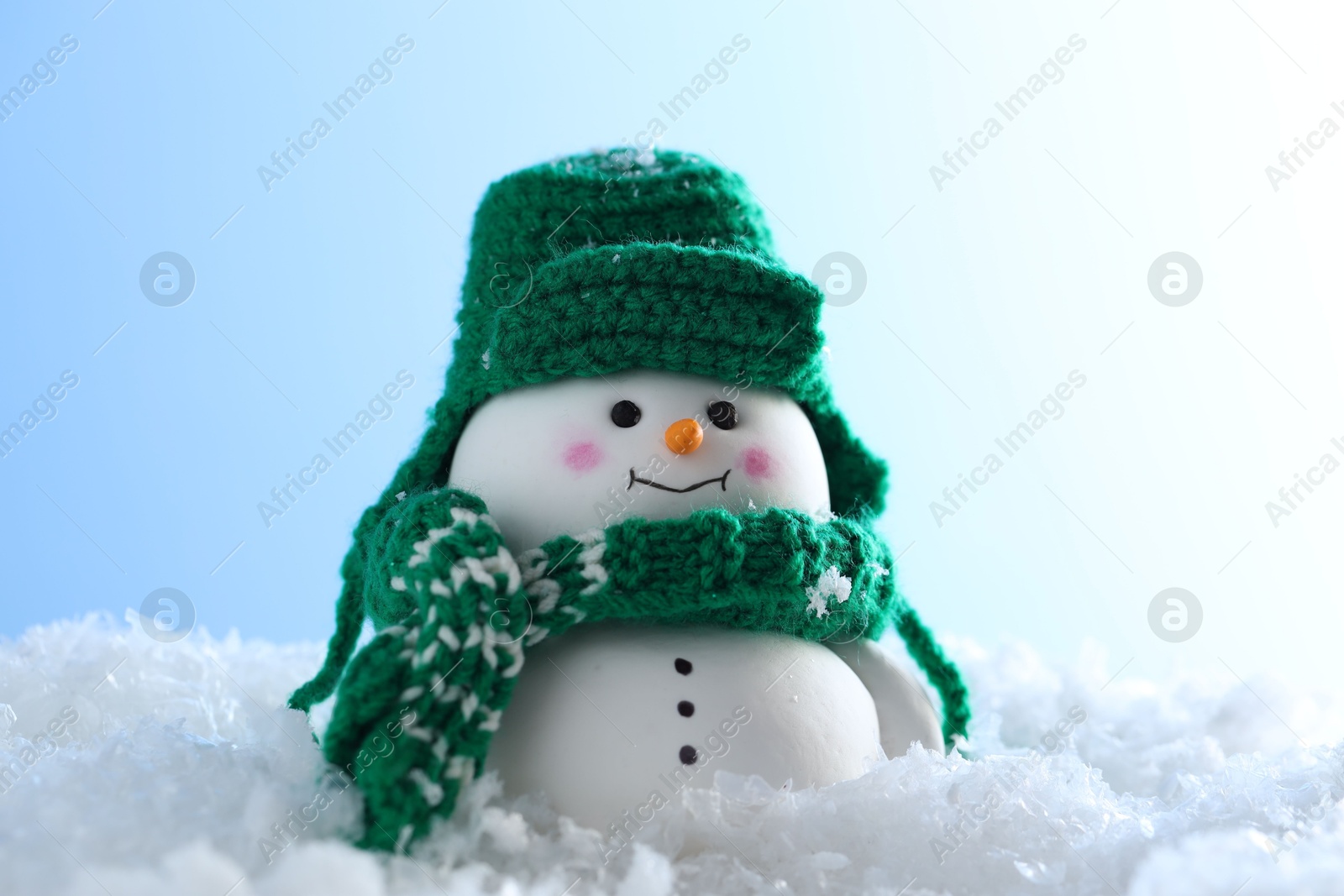 Photo of Cute decorative snowman on artificial snow against light blue background, closeup