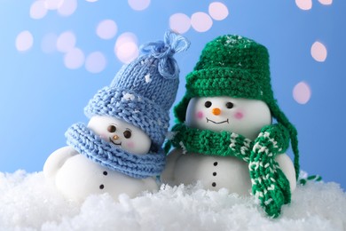 Photo of Cute decorative snowman on artificial snow against light blue background with blurred lights, closeup