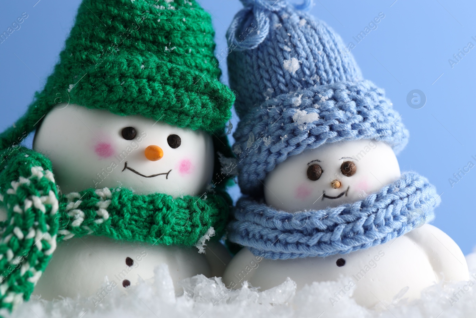 Photo of Cute decorative snowmen against light blue background, closeup