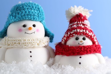 Photo of Cute decorative snowmen against light blue background, closeup