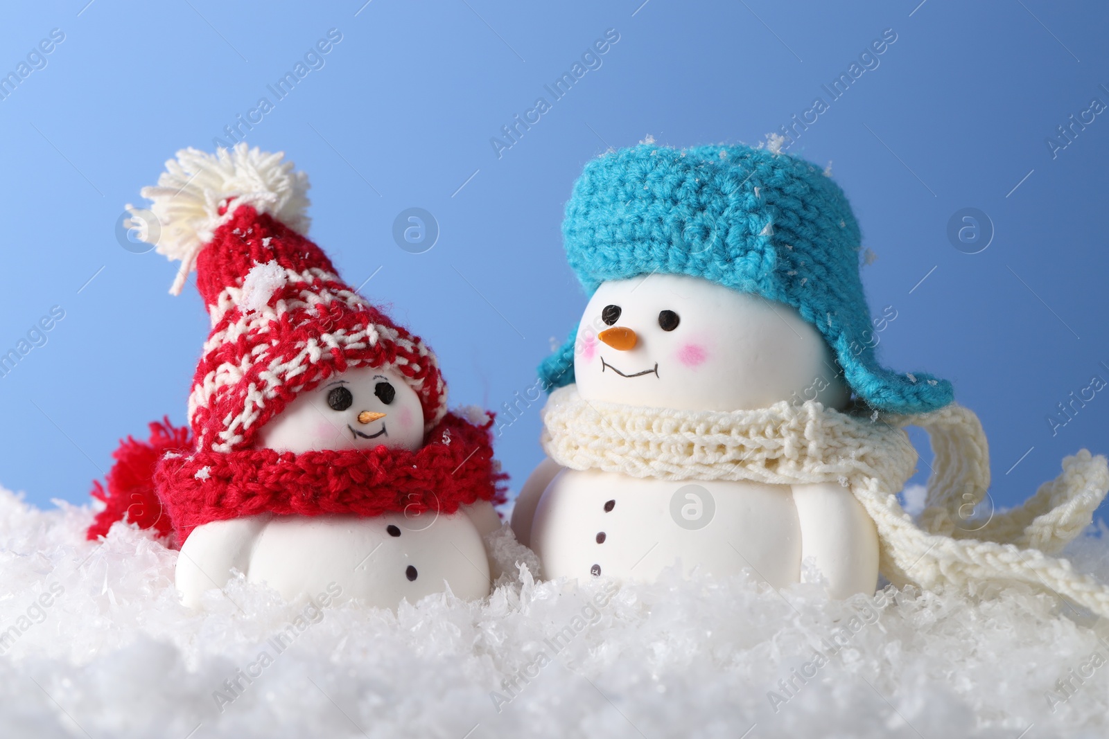 Photo of Cute decorative snowmen against light blue background, closeup