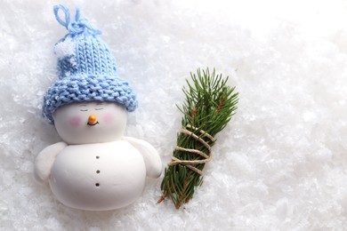 Photo of Cute decorative snowman and fir tree branches on artificial snow, flat lay