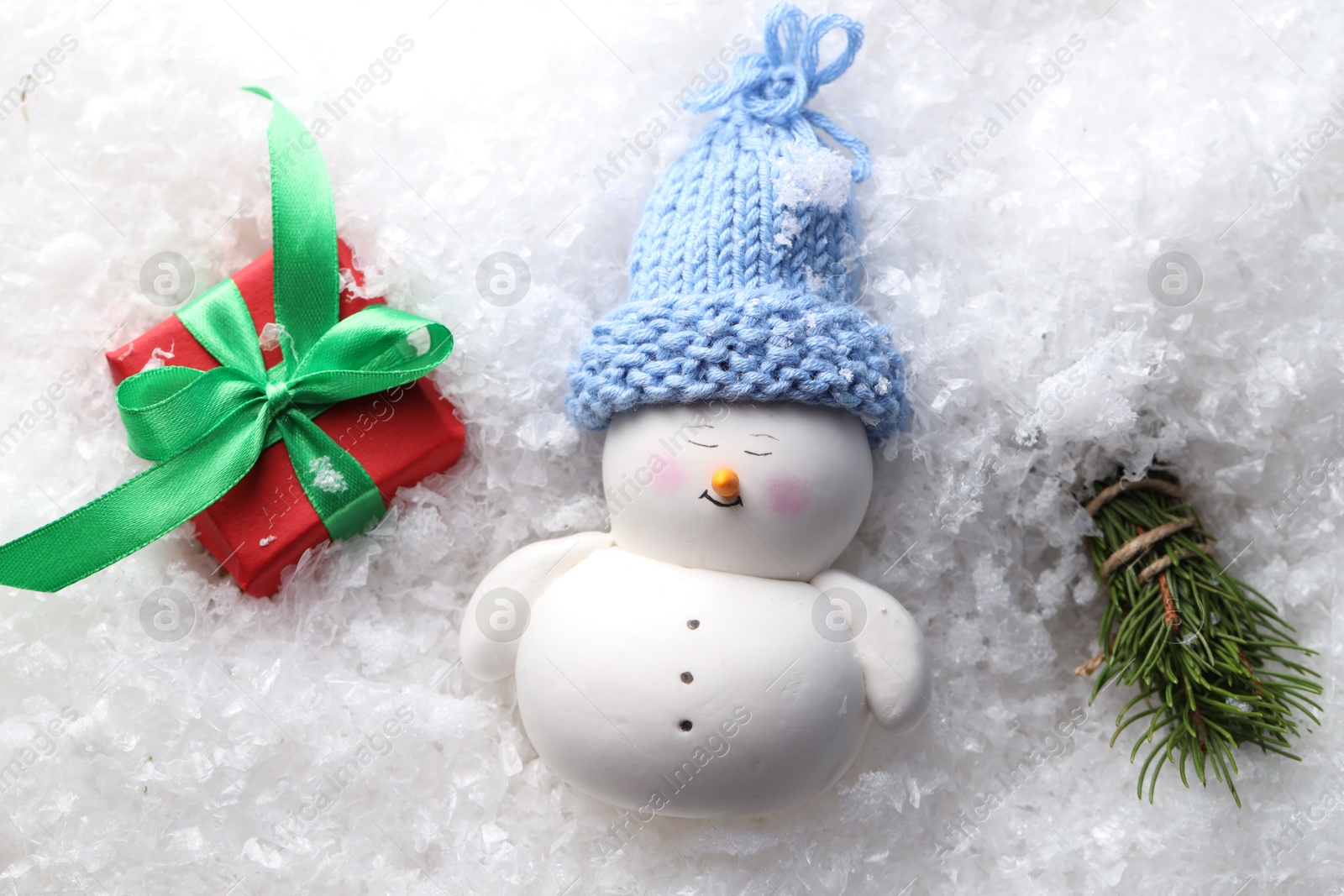 Photo of Cute decorative snowman, fir tree branches and gift box on artificial snow, flat lay