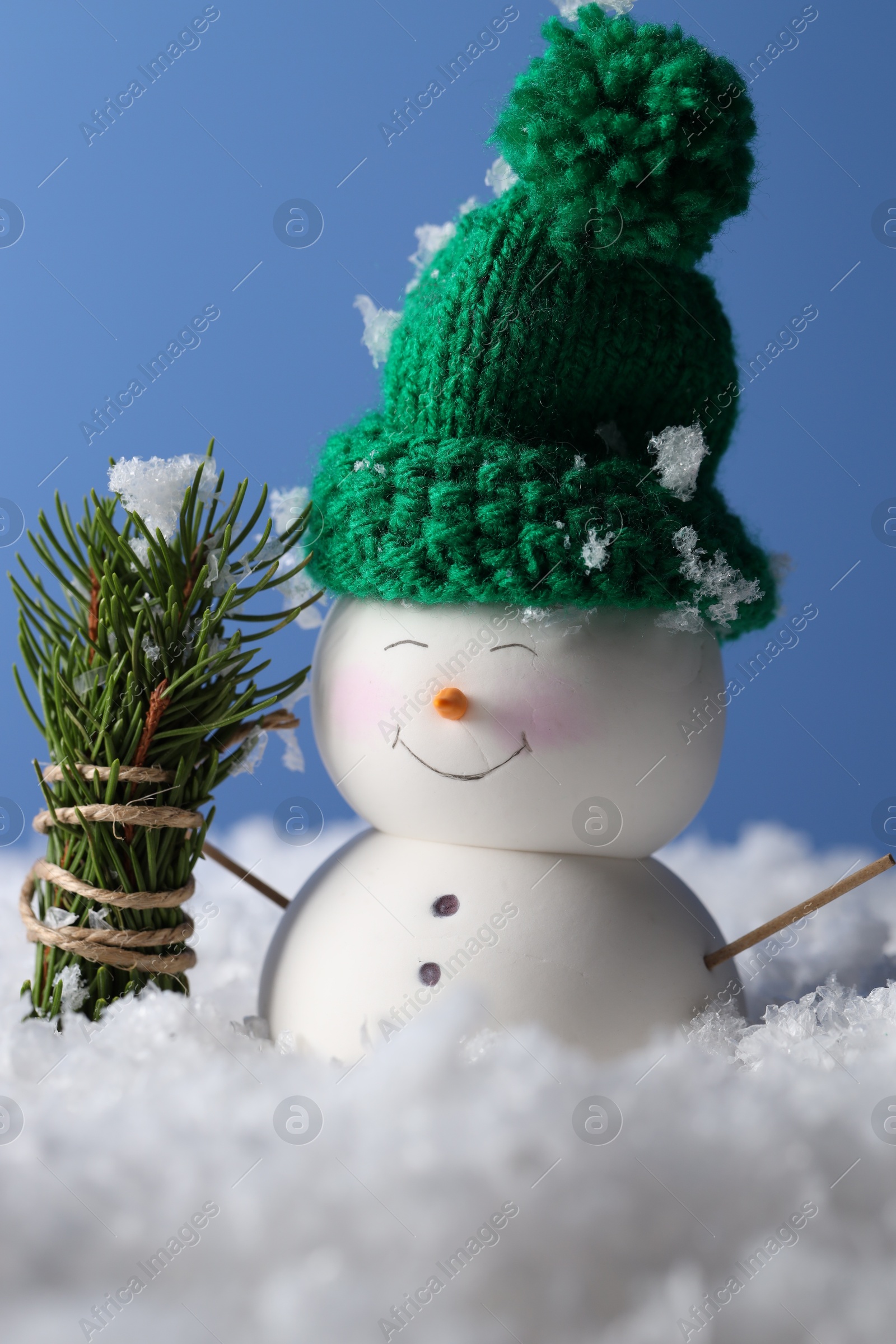 Photo of Cute decorative snowman and fir tree branches on artificial snow against light blue background, closeup