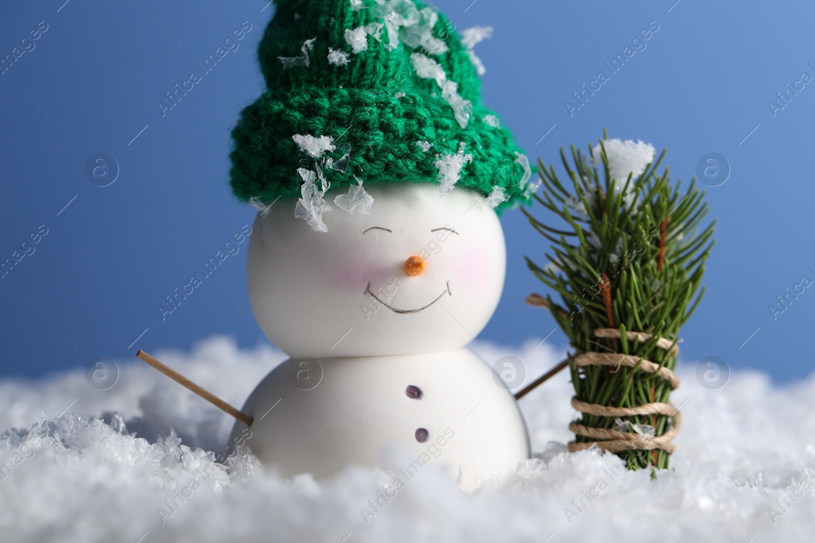 Photo of Cute decorative snowman and fir tree branches on artificial snow against light blue background, closeup