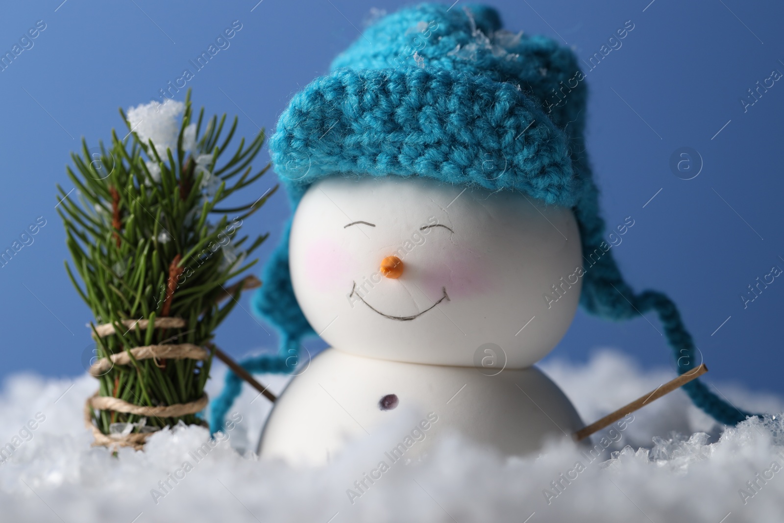 Photo of Cute decorative snowman and fir tree branches on artificial snow against light blue background, closeup